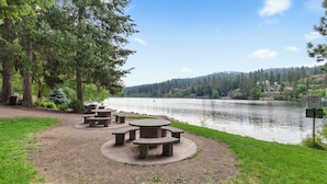 Un espace de pique-nique aménagé au bord du lac, avec des tables et des bancs en pierre, entouré d’arbres et offrant une vue dégagée sur le lac.