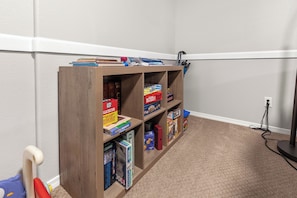 Un racó d'una habitació amb una biblioteca de fusta plena de jocs de taula i trencaclosques.