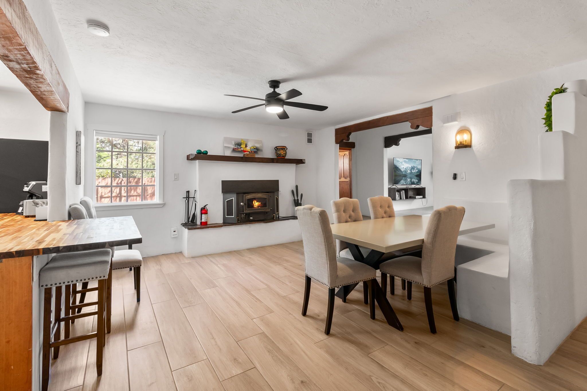 A modern kitchen with a fireplace, dining area with chairs, and a ceiling fan.