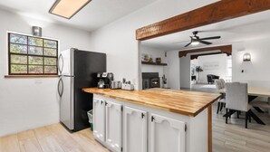 Una cocina moderna con encimera de madera, armarios blancos y un refrigerador negro, además de un comedor con mesa y sillas.