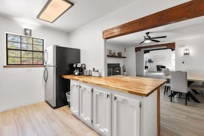 Eine moderne Küche mit Holzarbeitsplatte, weißen Schränken, einem schwarzen Kühlschrank und einem Essbereich mit Tisch und Stühlen.