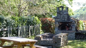 Un horno de piedra al aire libre, una mesa de picnic de madera y una valla de madera en un jardín.