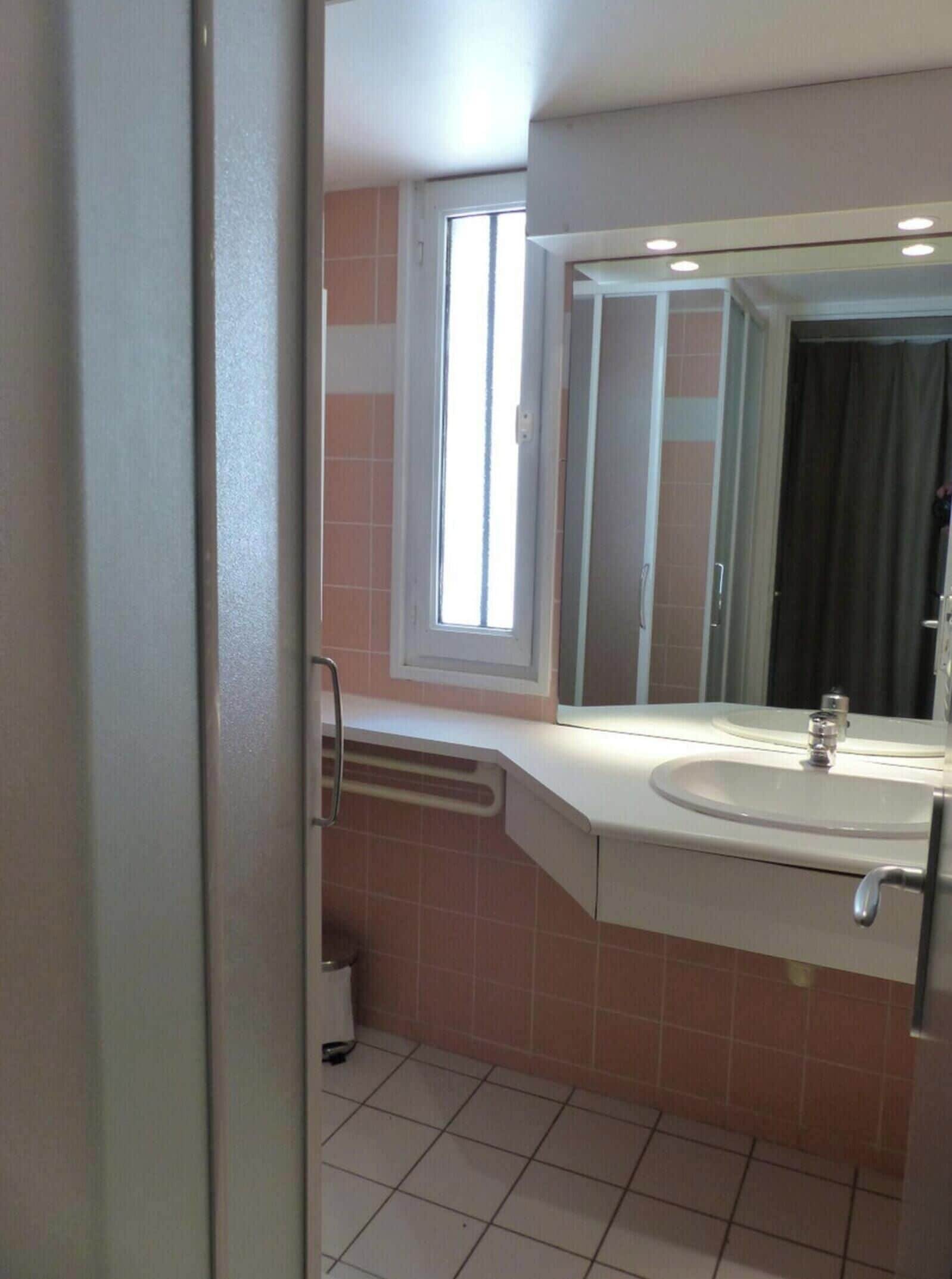 A bathroom with a sink, mirror, window, and a door.