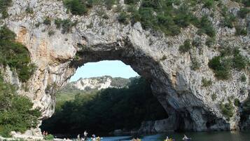 A natural rock arch formation with a river below and people kayaking.