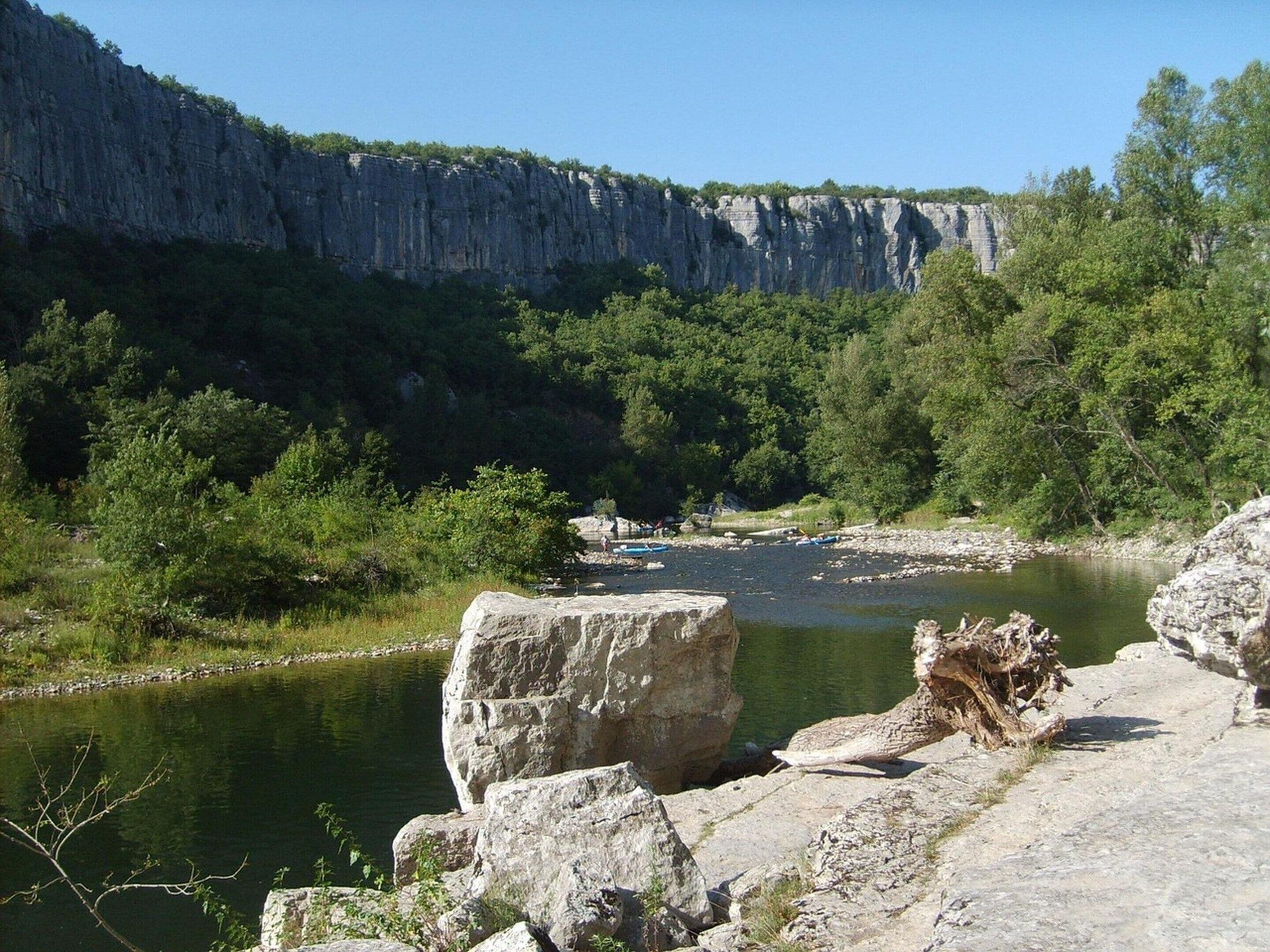 A river with boats, rocky terrain, and a cliff.