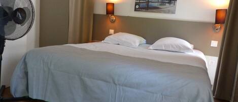 A hotel room with a large bed, two wall-mounted lamps, a ceiling fan, and a painting on the wall.