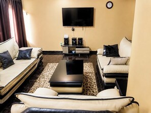 Ein Wohnzimmer mit zwei Sofas, einem Couchtisch, einem Flachbildfernseher und einer Wanduhr.
