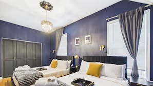 A hotel room with two beds, a chandelier, a large window with curtains, and a bedside table with a tray. - The Dakin Estate: A refined 4BR Art Deco speakeasy duplex in Wrigleyville. Featuring curated interiors, elevated finishes, and a private entertainment lounge just minutes from Wrigley Field, dining, nightlife, and Chicago’s iconic attractions. (Chicago)