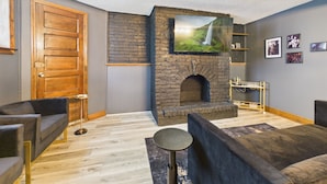 A cozy living room with a stone fireplace, comfortable seating, and a television mounted above it. - The Dakin Estate: A refined 4BR Art Deco speakeasy duplex in Wrigleyville. Featuring curated interiors, elevated finishes, and a private entertainment lounge just minutes from Wrigley Field, dining, nightlife, and Chicago’s iconic attractions. (Chicago)
