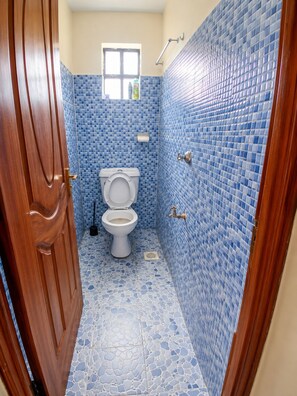 A bathroom with a toilet, a window, and blue mosaic tiles. - Beautiful and cozy odern bedroom unit in Mirema, Nairobi. 20 min drive from CBD. (Nairobi)