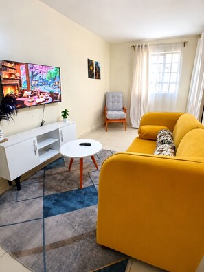A living room with a sofa, armchair, TV, and a small table. - Beautiful and cozy odern bedroom unit in Mirema, Nairobi. 20 min drive from CBD. (Nairobi)