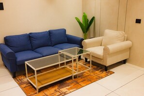 Un canapé bleu, un canapé blanc et une table basse en verre dans une pièce où se trouve un tapis à motifs.
