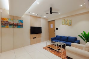 A modern living room with a blue sofa, a white armchair, a coffee table, a flat-screen TV, and a ceiling fan.