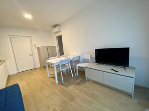 A room with a dining table, chairs, a TV on a stand, a white cabinet, and a door. - Bright Flat With Spacious Terrace Near the sea (San Michele al Tagliamento)