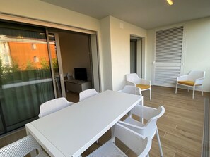 Ein Balkon mit weißem Tisch und Stühlen, einem Fernseher und einer Schiebetür.