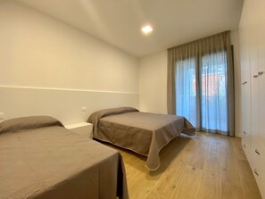 Ein Zimmer mit zwei Betten, einem Vorhangfenster und einem Kleiderschrank.