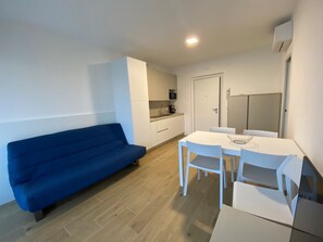 A compact living space with a sofa, a dining table with chairs, a kitchenette, and a door. - Bright Flat With Spacious Terrace Near the sea (San Michele al Tagliamento)