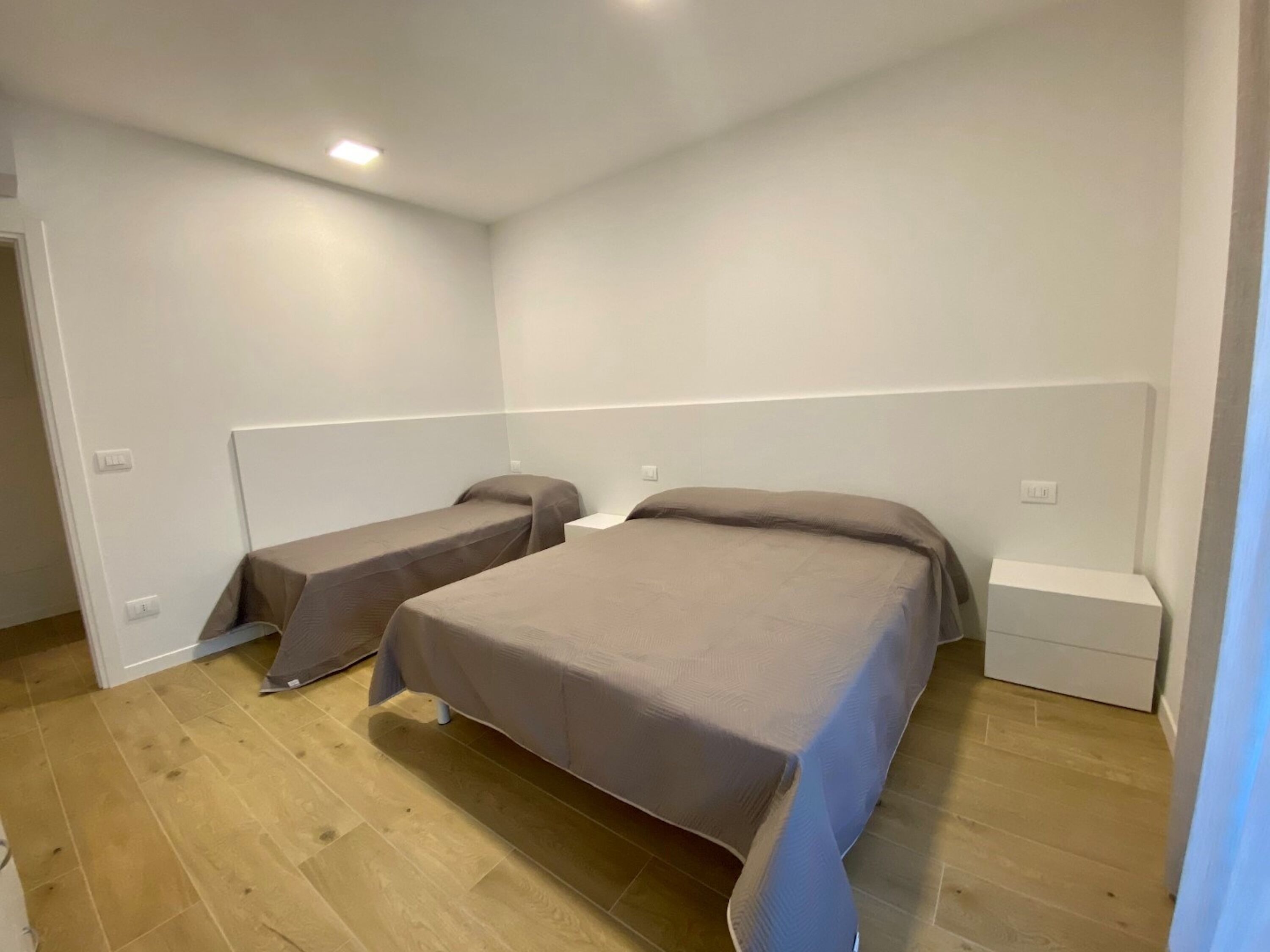 A room with two beds, a white headboard, and a wooden floor.