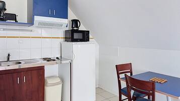 Een kleine keuken met een witte koelkast, een magnetron, een spoelbak en een eettafel met stoelen.