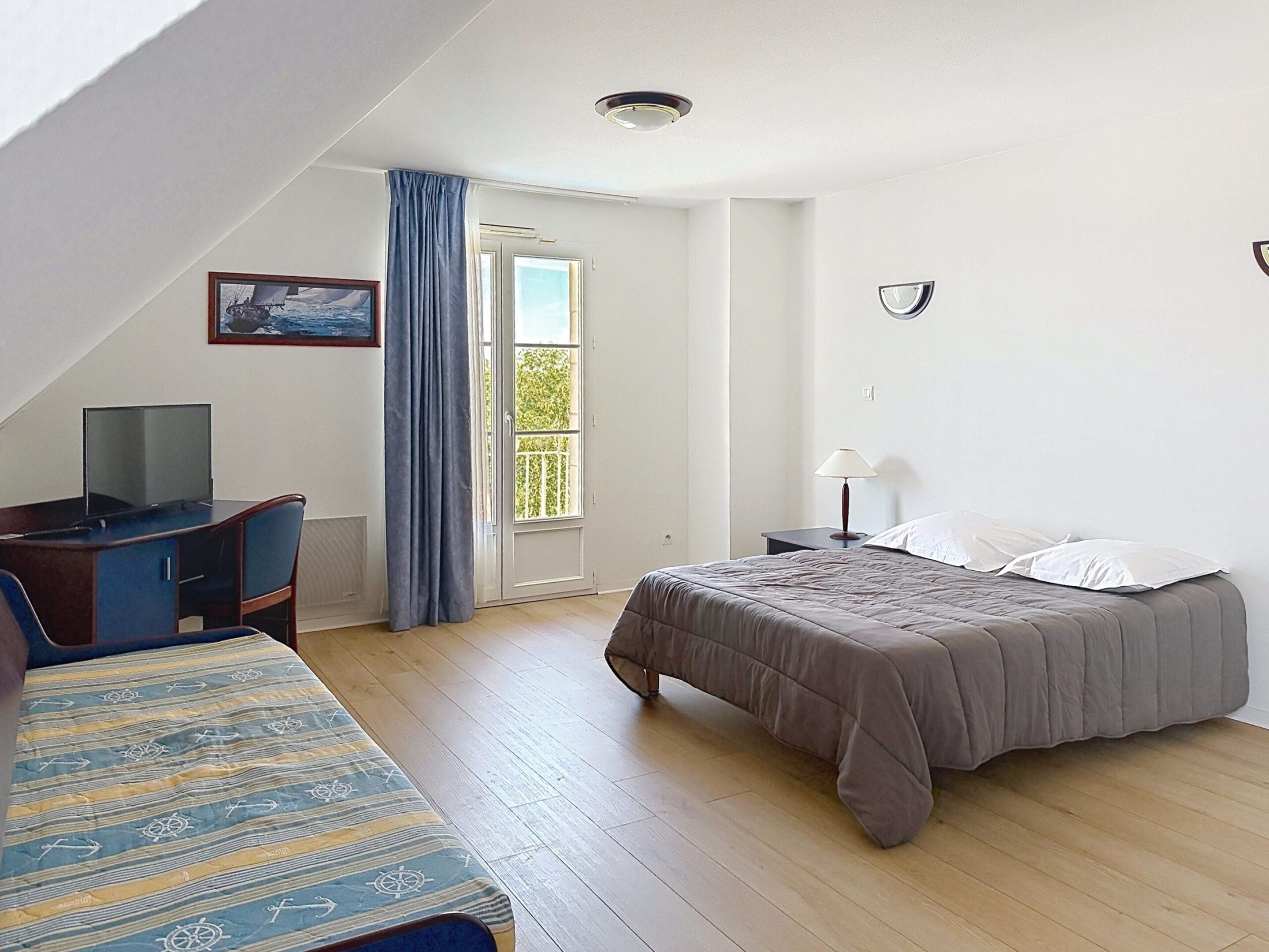 A bedroom with a bed, a desk, a television, and a window with curtains.