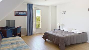 A bedroom with a bed, a desk, a television, and a window with curtains.