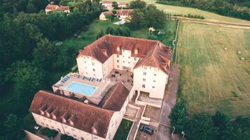 An aerial view of a large estate with multiple buildings, a swimming pool, and surrounding green fields.