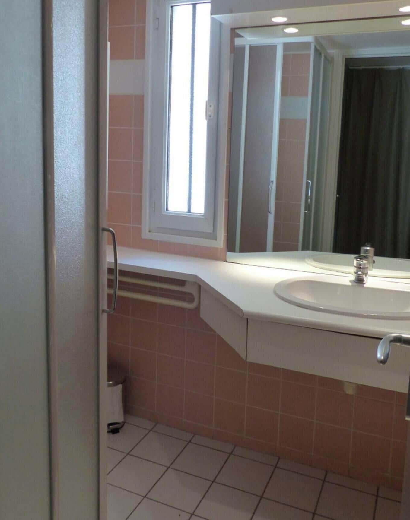 Un baño con lavamanos, espejo, ventana y puerta.