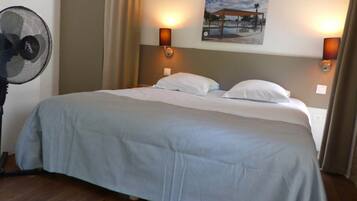 Een hotelkamer met een bed, twee wandlampen, een plafondventilator en een schilderij aan de muur.