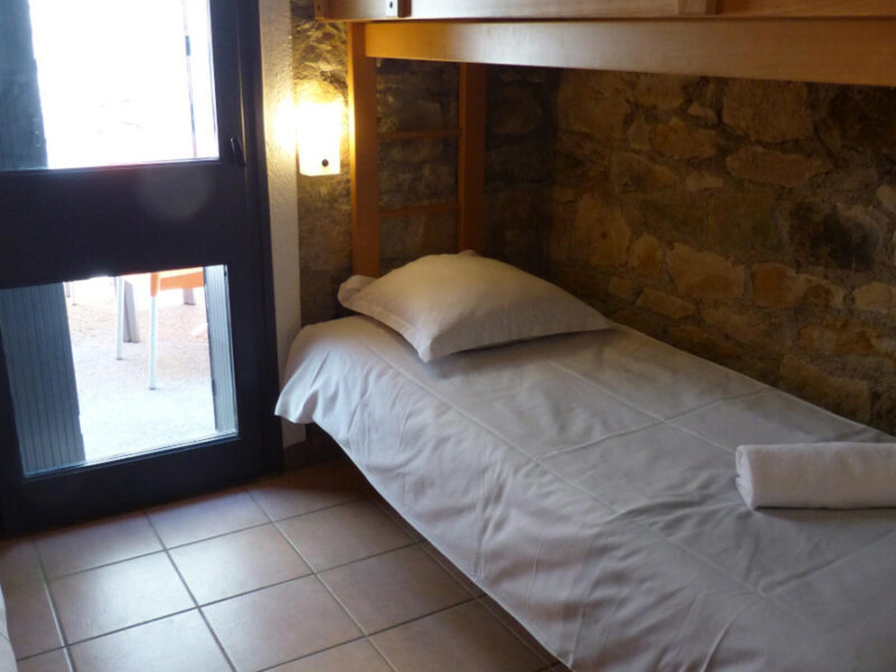 A single bed with white bedding in a room with stone walls and a window.