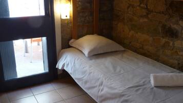 A single bed with white bedding in a room with stone walls and a window.