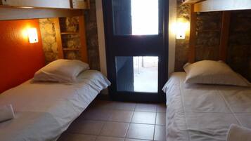 A room with two beds, a stone wall, a wooden door, and a window.