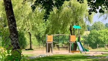 Un terrain de jeux avec un toboggan et des structures d’escalade, entouré d’arbres et d’herbe.