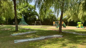 Ein Park mit Spielgeräten, darunter Schaukeln und Rutschen, umgeben von Bäumen.