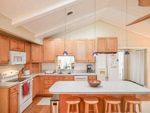 Eine moderne Küche mit Holzausstattung, einer zentralen Kochinsel mit Sitzgelegenheiten, einer Mikrowelle, einem Herd und einem Kühlschrank.