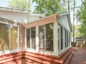 Eine überdachte Veranda mit Holzterrasse, großen Fenstern und einer weißen Außenwand.