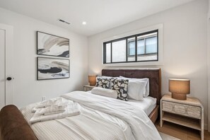 Un dormitorio con una cama grande, dos mesitas de noche, un ventanal con persianas y una obra de arte abstracta en la pared.
