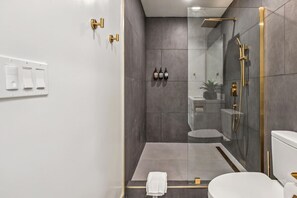 A modern bathroom with a glass-enclosed shower, a white toilet, and a small sink. - Spacious 5BR Getaway –Clean, Comfortable, Relaxing (Daly City)