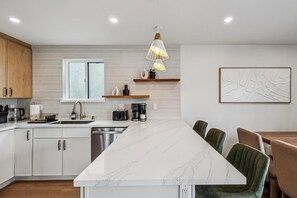 Una cocina moderna con armarios blancos, una isla de mármol e iluminación colgante.