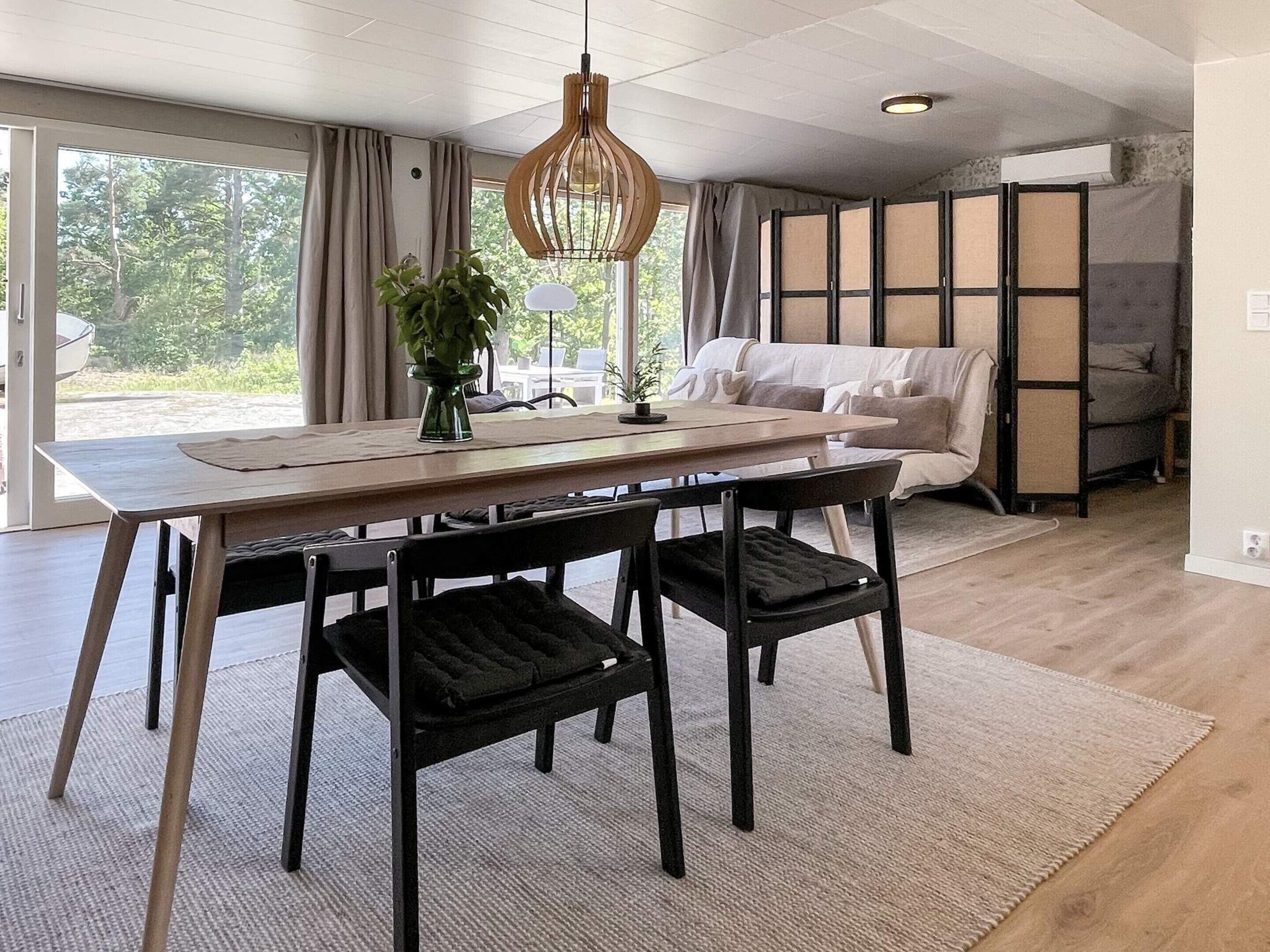 Et moderne opholdsrum med spiseplads, sofa, et stort vindue med gardiner og udsigt til grønne områder.