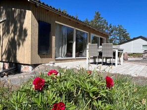 A modern wooden building with large windows, outdoor seating, and a garden with red flowers. - 4 Star Holiday Home in Oskarshamn (Oskarshamn)