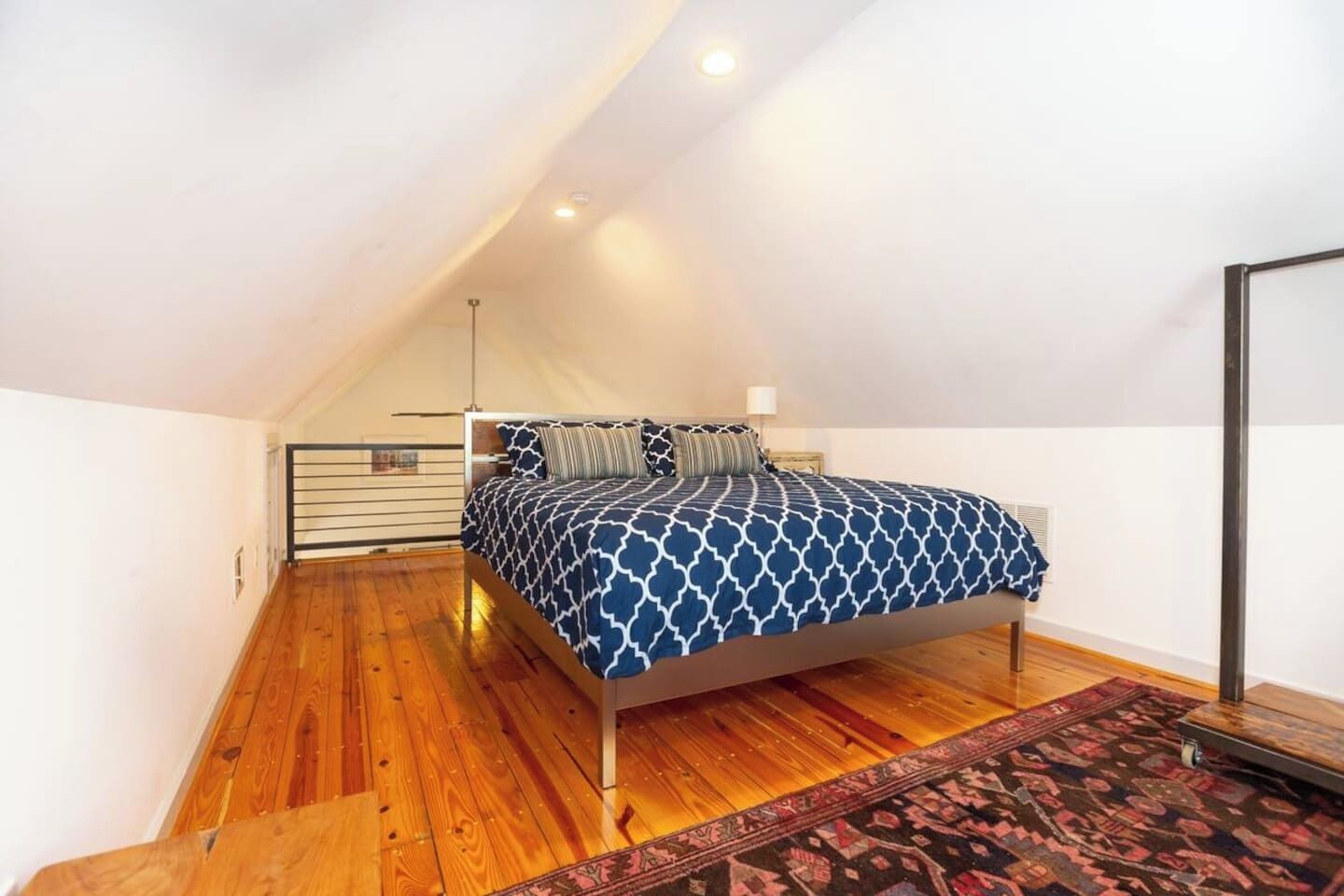 Un dormitorio con techo inclinado, una cama con ropa de cama estampada, piso de madera y una alfombra.