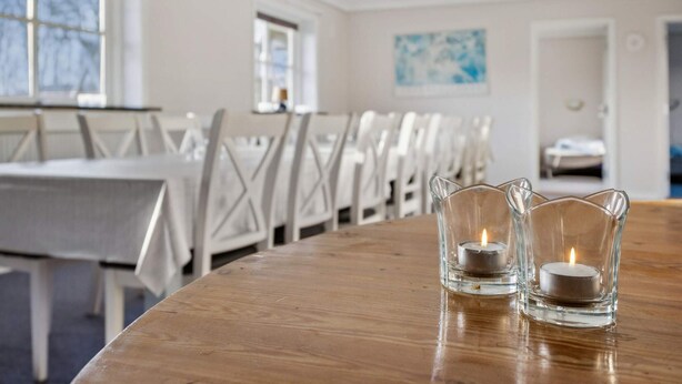 A conference room with a long wooden table, white chairs, and two lit candles on the table. - 20 Person Holiday Home in Norre Nebel (Norre Nebel)
