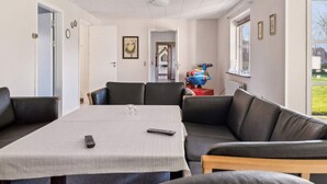 A modern living room with a large sofa, a dining table, and a colorful toy on a side table. - 20 Person Holiday Home in Norre Nebel (Norre Nebel)