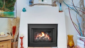 Ein Kamin mit Kaminvorsatz, eine Holzschrank und ein Bild an der Wand.