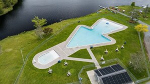 Ein Pool mit ungewöhnlicher Form, umgeben von einem eingezäunten Bereich mit Rasen und einigen Bäumen.