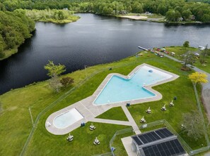 Ein Pool mit ungewöhnlicher Form, umgeben von einem eingezäunten Bereich mit Rasen und einigen Bäumen.