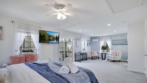 Ein Schlafzimmer mit Bett, Deckenventilator, Fernseher und Blick auf eine Terrasse.