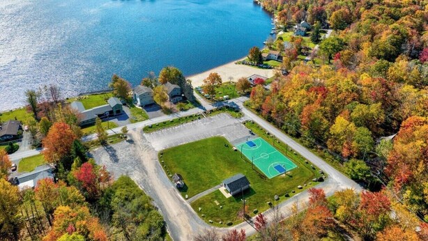 Luftaufnahme einer Wohngegend am Seeufer mit Häusern, einem Basketballplatz und herbstlicher Laubfärbung.