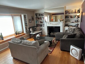 Ein Wohnzimmer mit Kamin, einer Couch, einem Sessel, einem Couchtisch und einem Bücherregal.