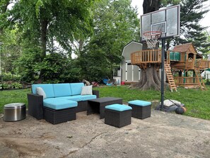 Eine Terrasse mit Gartenmöbeln, einem Basketballkorb und einem Baumhaus.